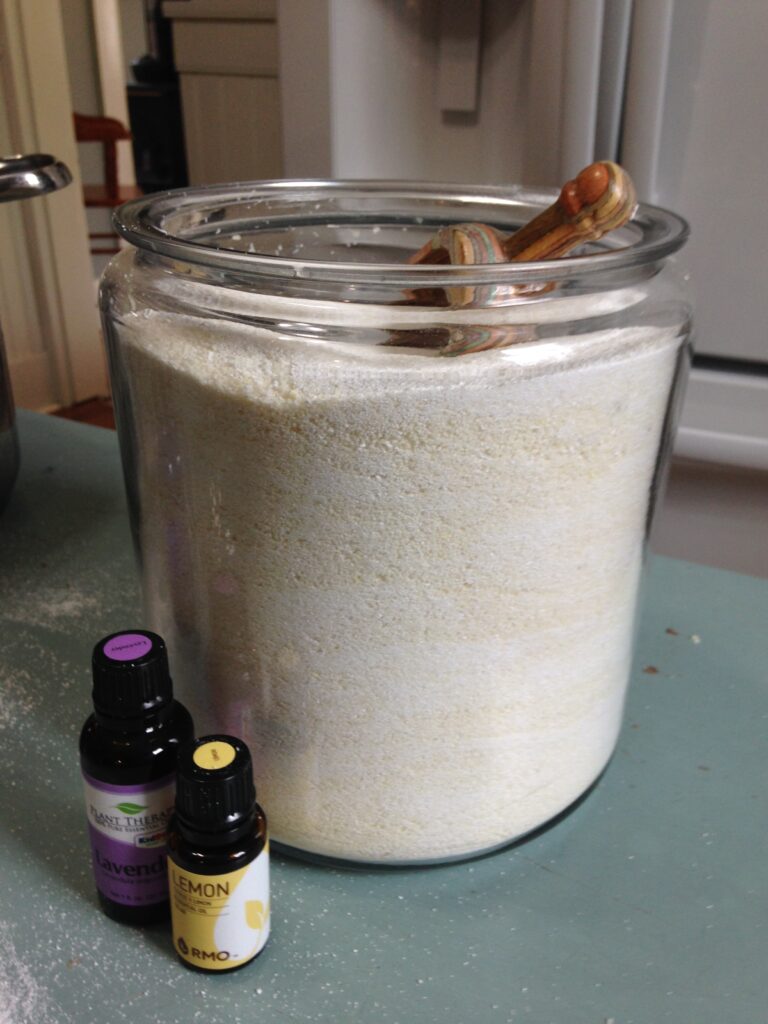 jar of powdered laundry soap with scoop and essential oil bottles on a blue table