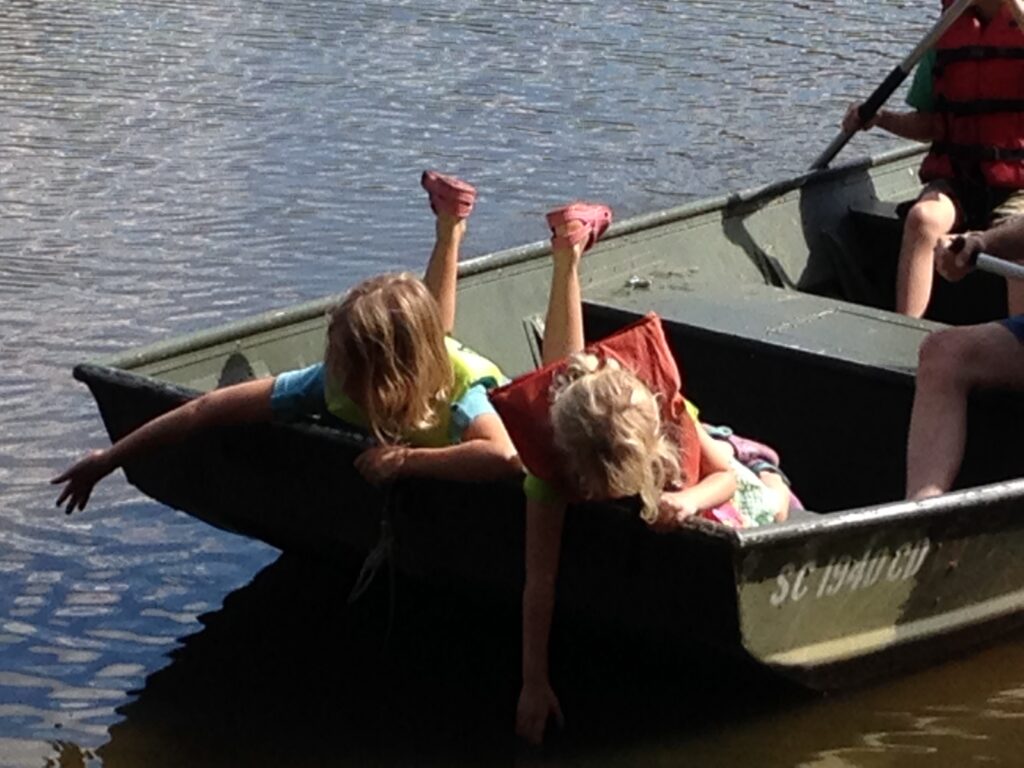 two girls leaning over into the water from the back of a rowboat experiencing Hygge in the summertime with family