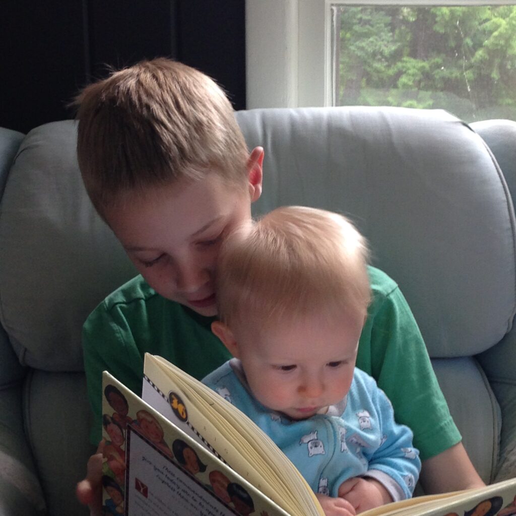 older boy reading a book to his little brother on his lap
