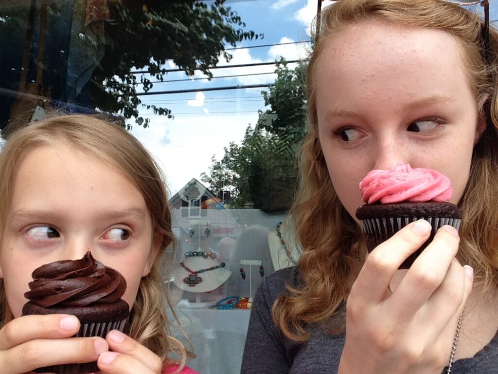 two girls looking at each other behind cupcakes