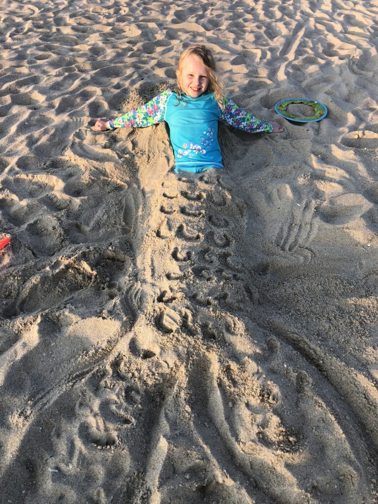 little girl on the beach covered in sand with a mermaid tail