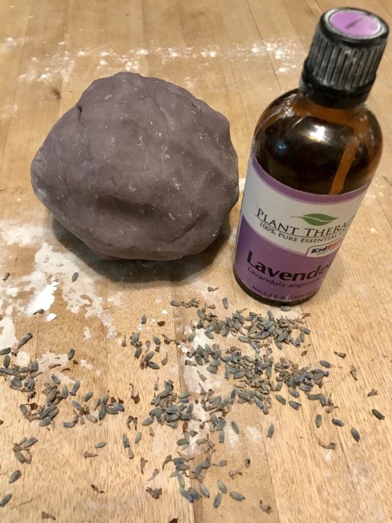 a purple ball of play dough by a bottle of lavender essential oil
