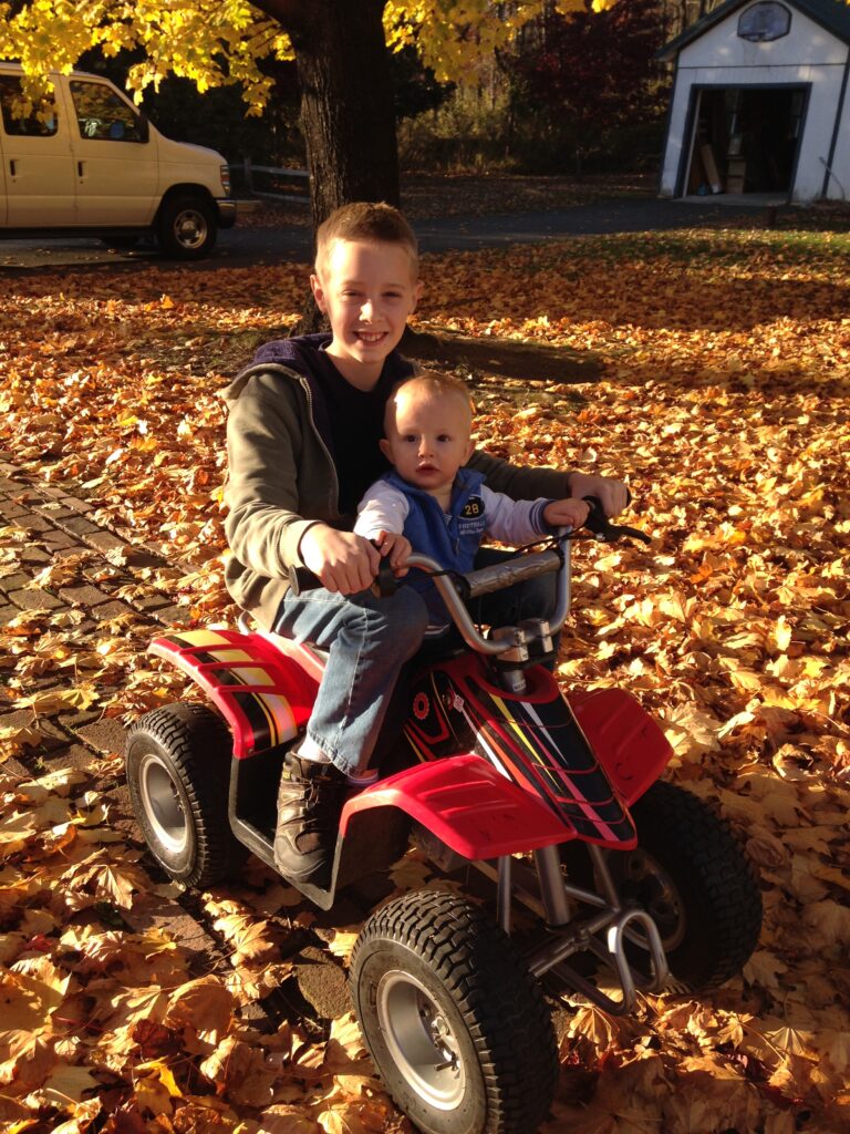 two boys on a 4 wheeler in the leaves