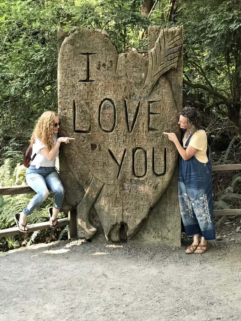 2 woman posed by a stone heart that reads I love you