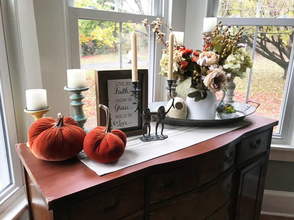 velvet pumpkins, candles, flowers and a sign on a buffet in front of a window