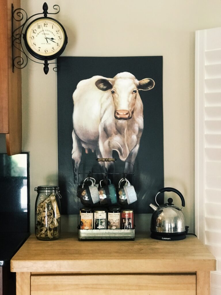 a mug tree with jar of biscotti and a tea pot with a cow picture behind it.