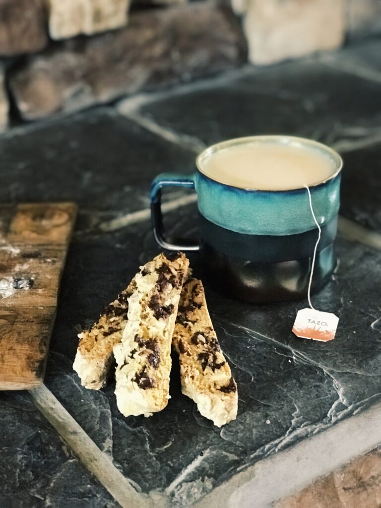 a mug of tea with 3 chocolate almond biscotti and a board on a slate surface