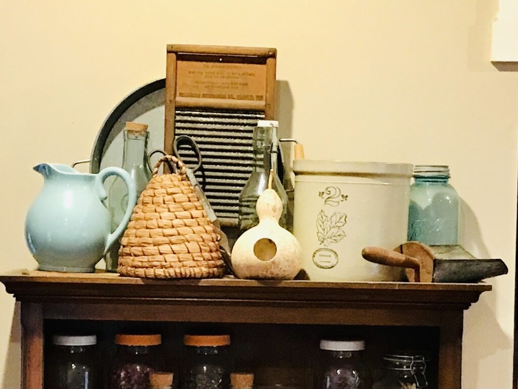 picture, washboard, beehive, birdhouse chord, shovel, aqua glass and crock on shelf