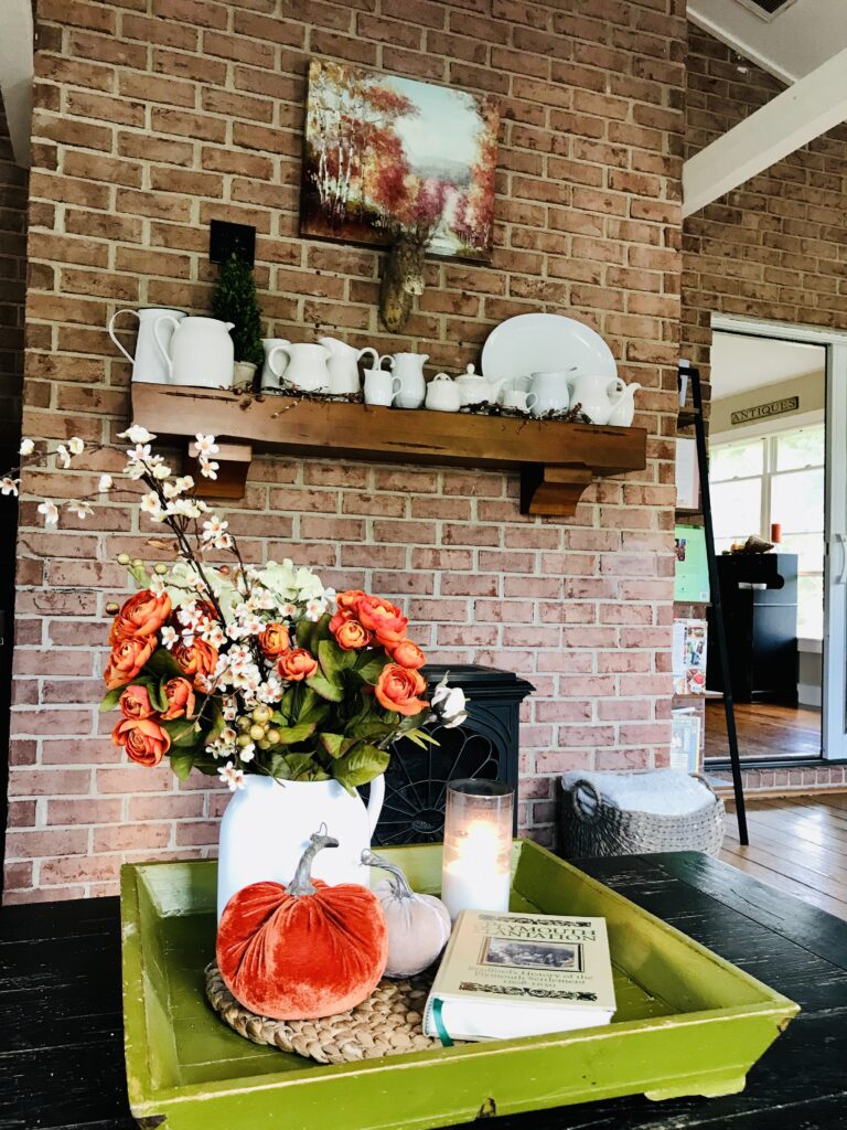 fall flowers, velvet pumpkins and a candle on a green tray with the backdrop of a brick wall and white pitchers
