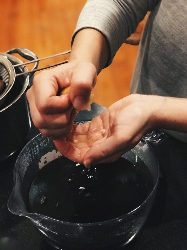 squeezing a lemon into a hand over a bowl of elderberry syrup