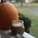 a jar of caramel sauce next to a pumpkin with a spoon dripping with caramel