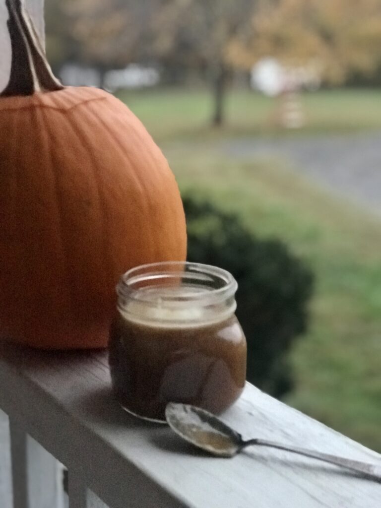 a jar of caramel sauce next to a pumpkin with a spoon dripping with caramel