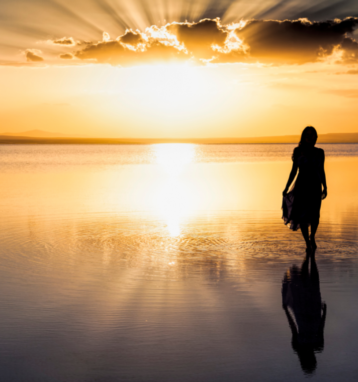 a woman walking on the water at sunset with reflection