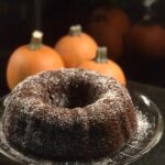 a chocolate bundt cake with 3 pumpkins on a black counter