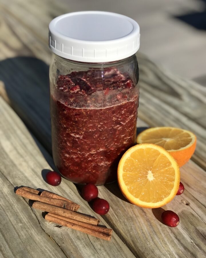 chutney in a jar on a wood table with orange, cinnamon stix, and cranberries