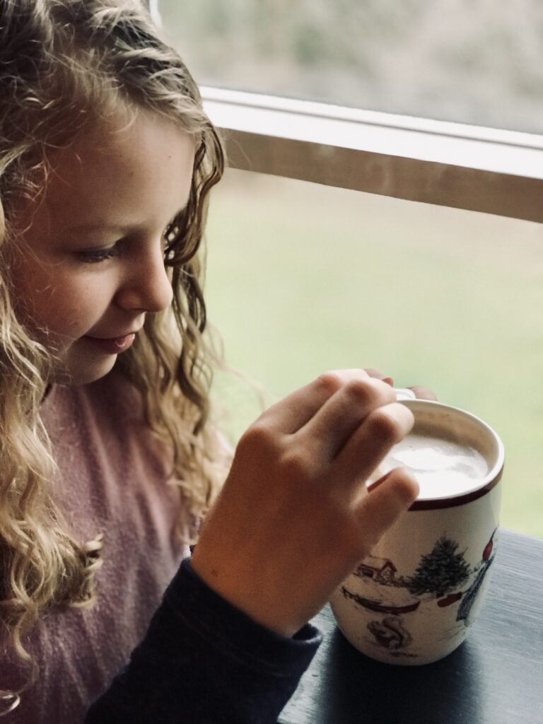 girl stirring hot chocolate by a window