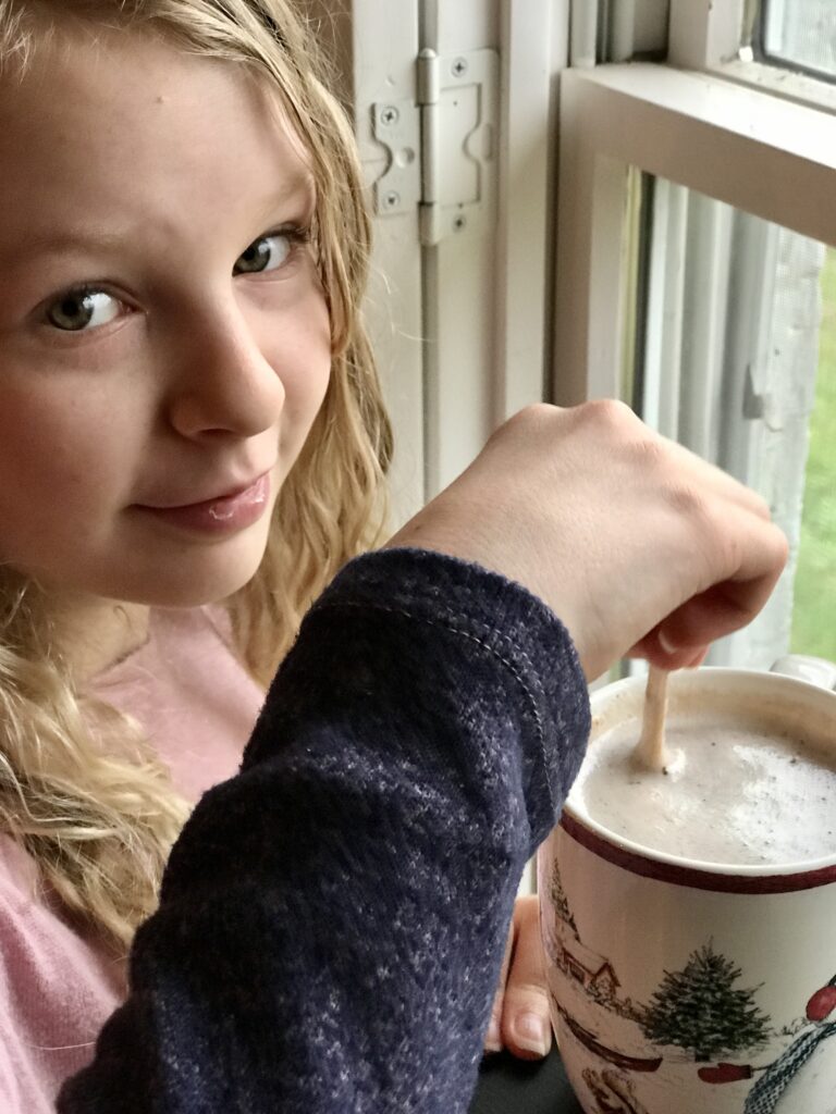 girl stirring her hot chocolate by the window