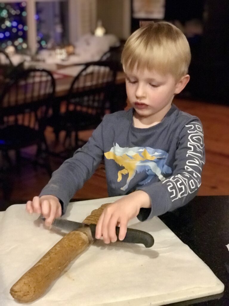boy cutting a cookie dough log