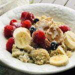 bowl of quinoa with berries, bananas, cinnamon and cream by a window