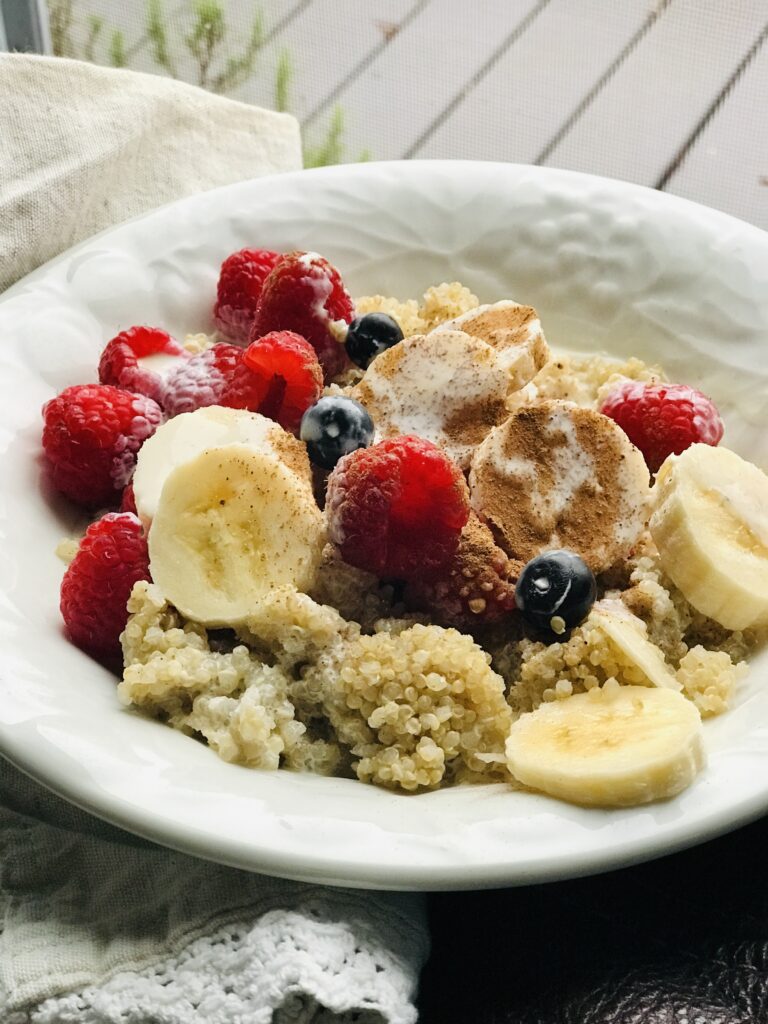 bowl of quinoa with berries, bananas, cinnamon and cream by a window