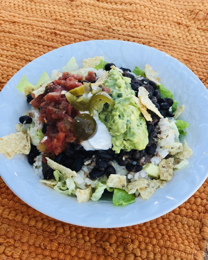 a bowl of rice, beans, guacamole on an orange tablecloth