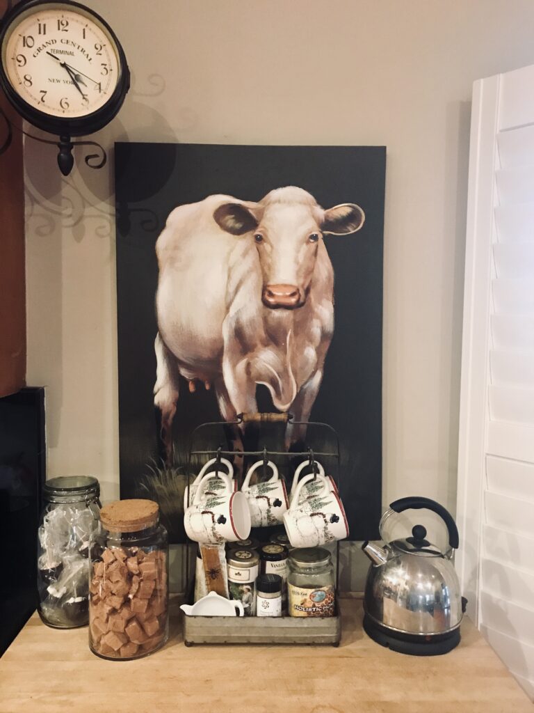 Hot chocolate station with mugs, marshmallows, a tea kettle, a clock and a picture of a cow