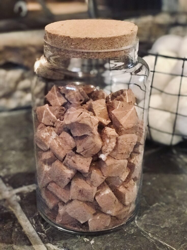 a jar of cocoa dusted homemade marshmallows by the fire with snowballs in the background