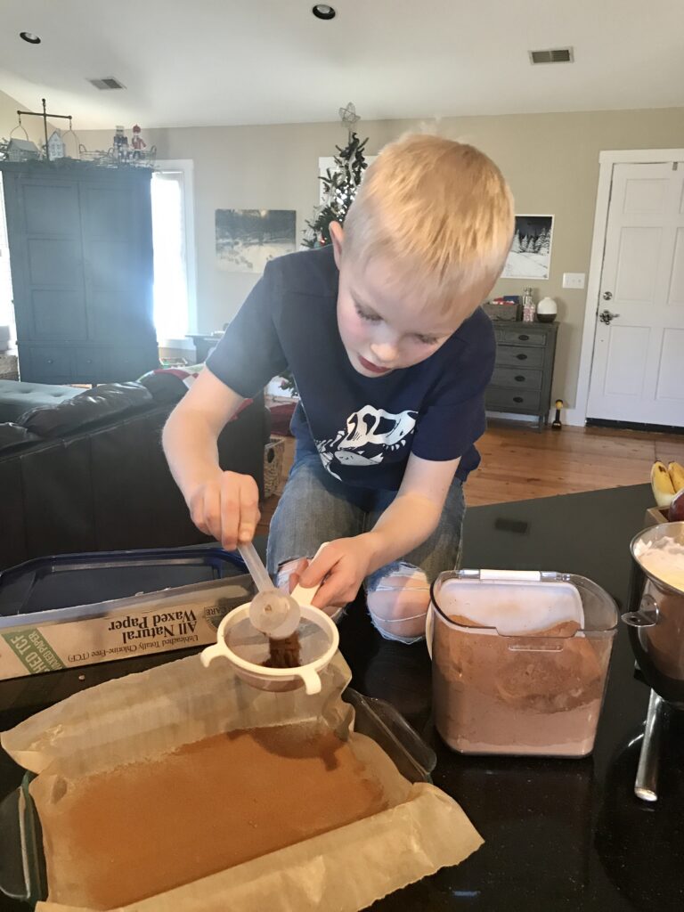 boy preparing a pan by dusting it with cocoa powder