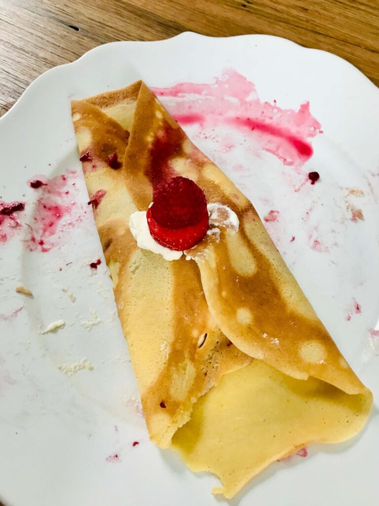 a single crepe on a white plate dotted with a raspberry