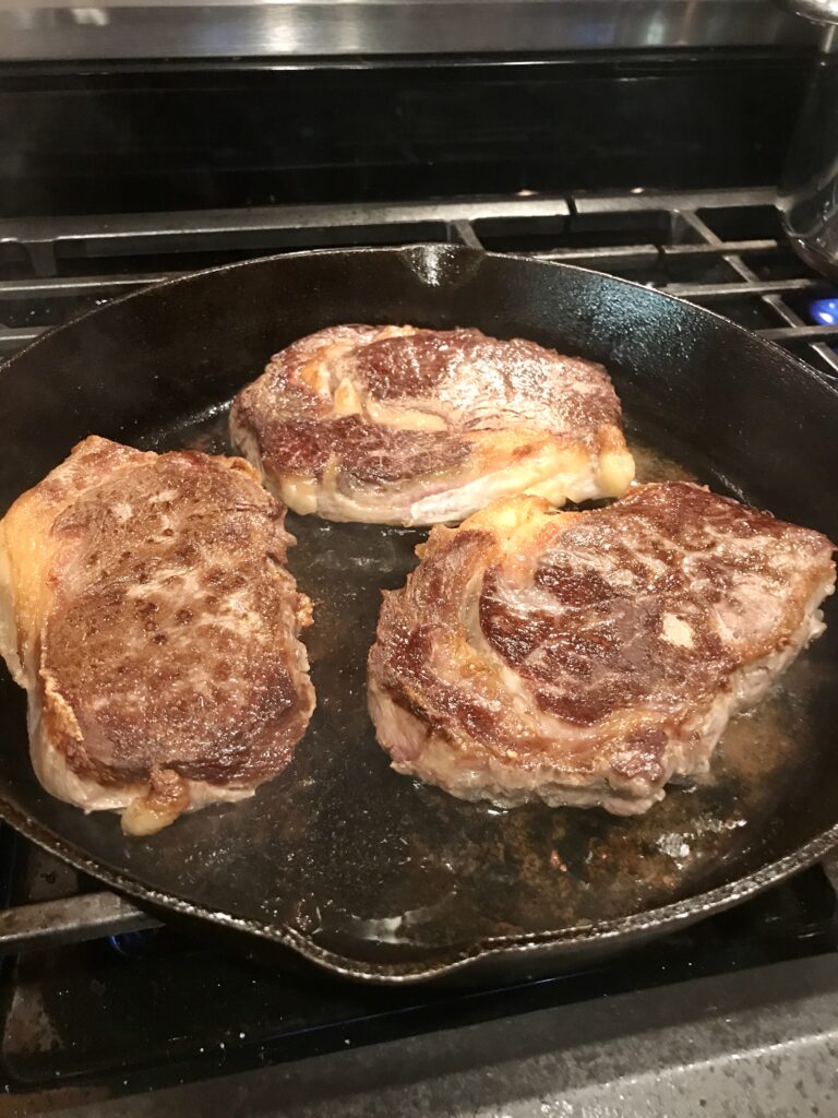 steaks searing in a cast iron pan
