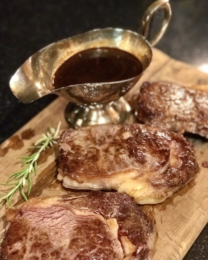 3 steaks on a breadboard with pan sauce