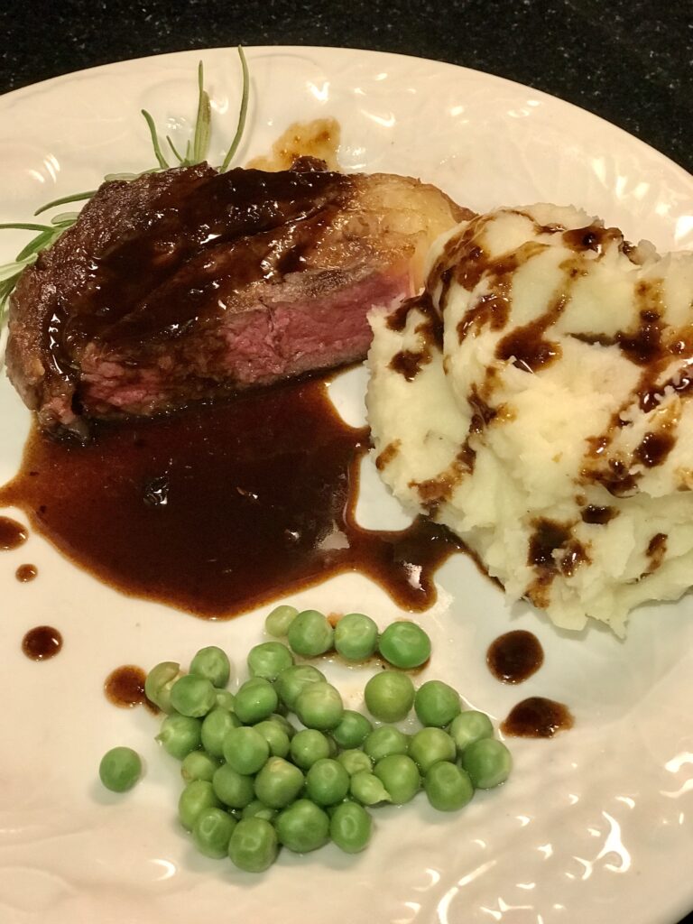 a steak plated with mashed potatoes and peas and pan sauce