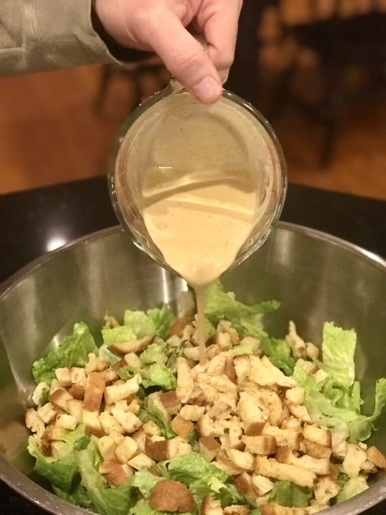 Caesar salad Dressing being poured onto a salad