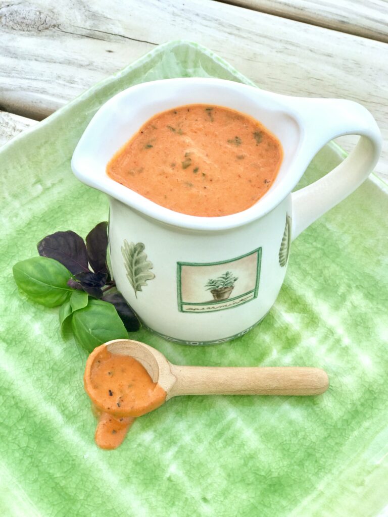 pitcher of roasted red pepper pasta sauce on a green platter with wooden spoon