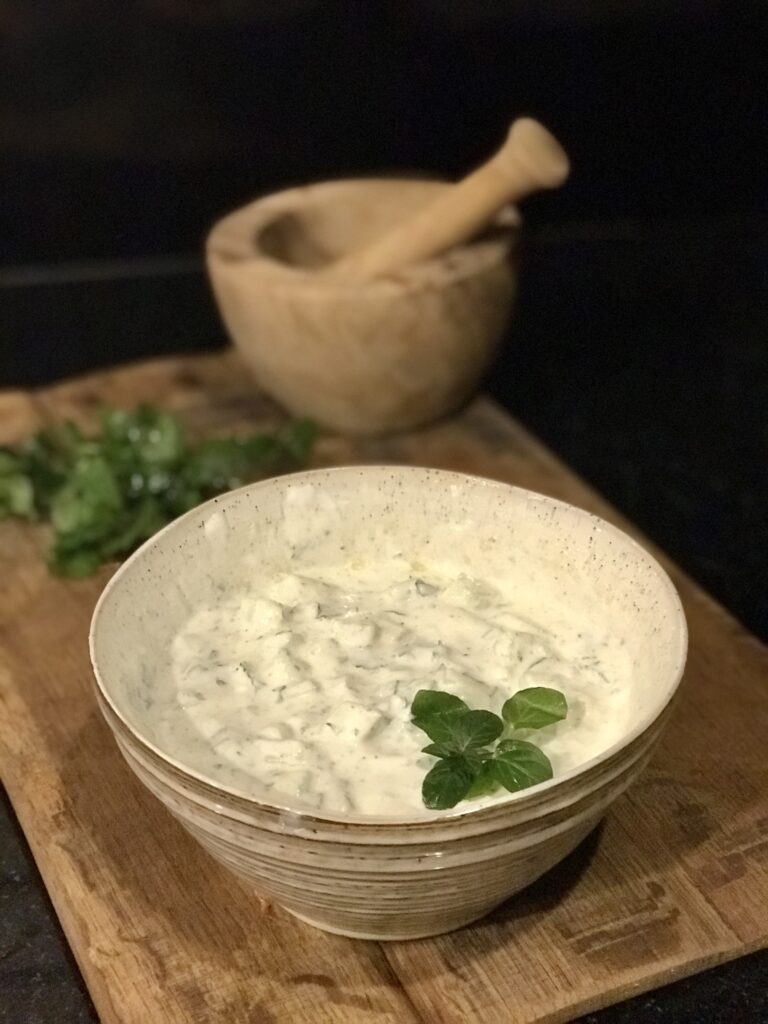 a bowl of Tzatziki sauce with a mortar and pestal in the background