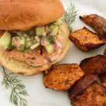 salmon burger with cucumber mustard sauce on a plate with cajun sweet potato wedges