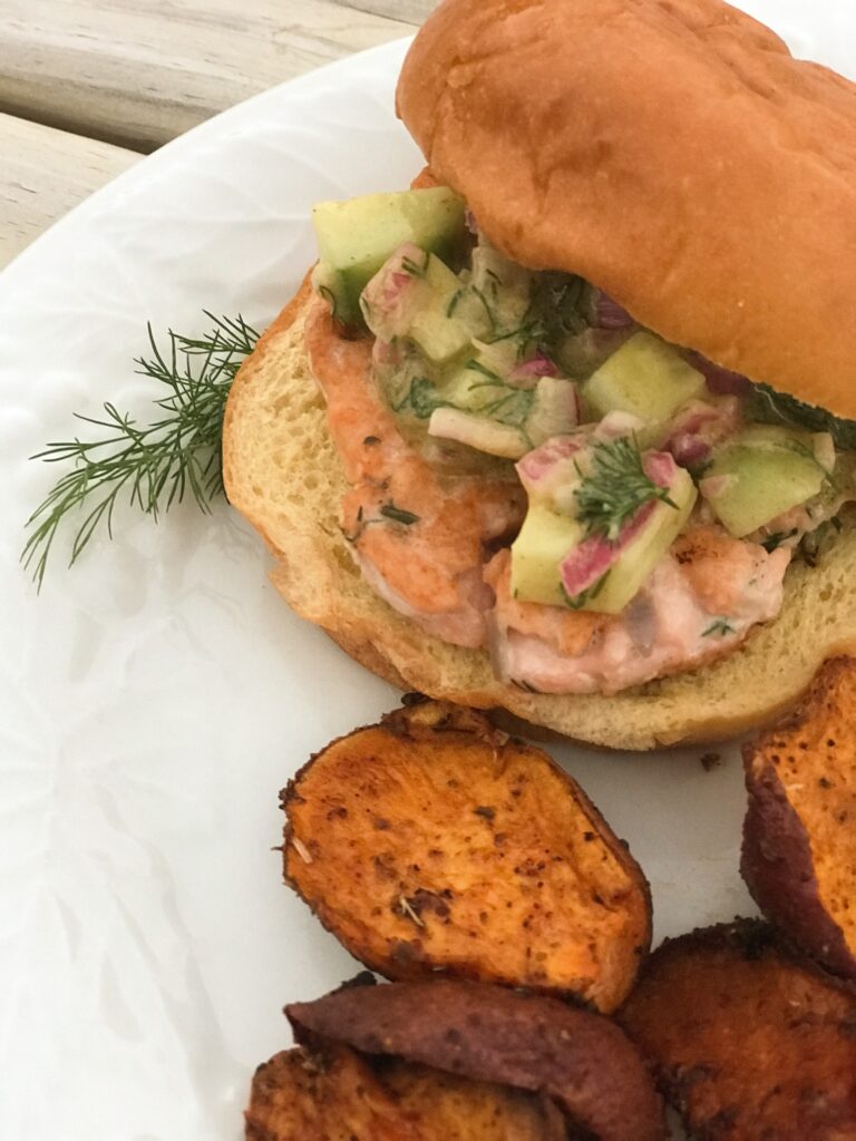 salmon burger  with sweet potato wedges on a white plate