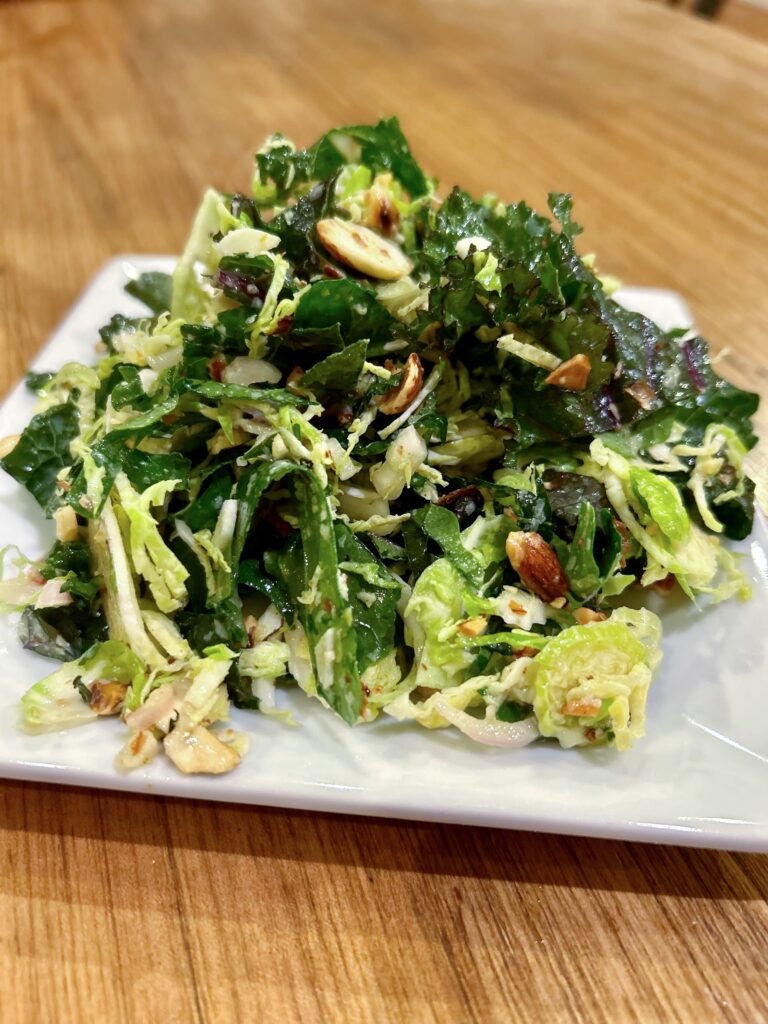 a white plate with kale & Brussels sprout salad with toasted almonds.