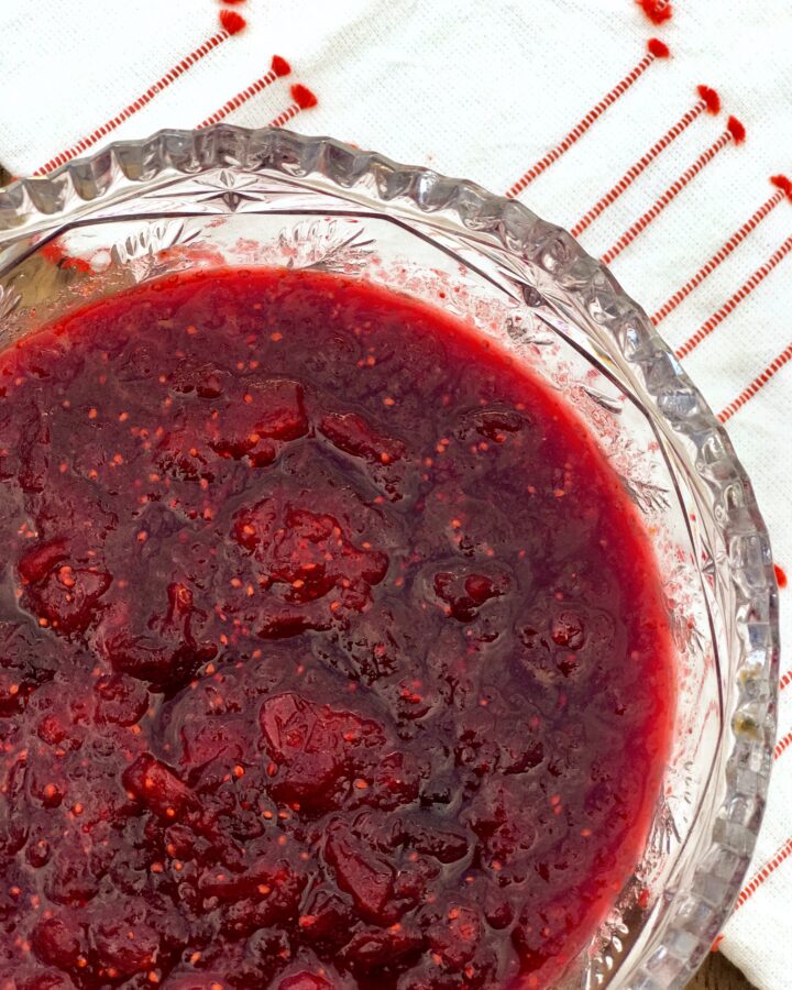a bowl of cranberry hibiscus sauce with a red and white towel underneath