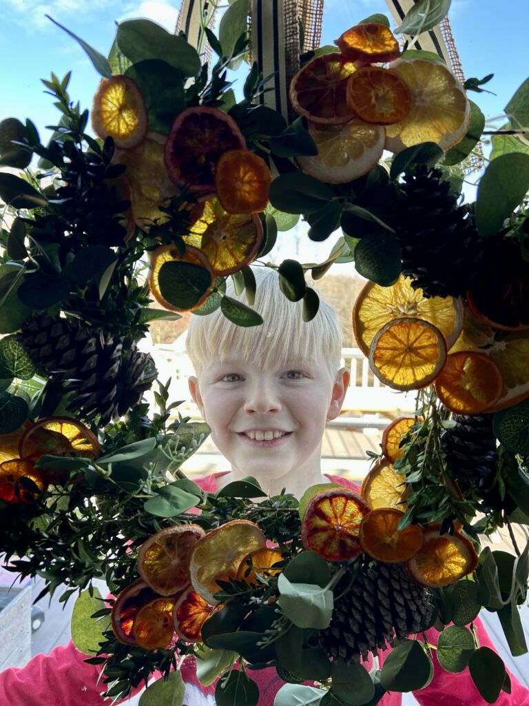 boy in the middle of an orange & eucalyptus winter wreath