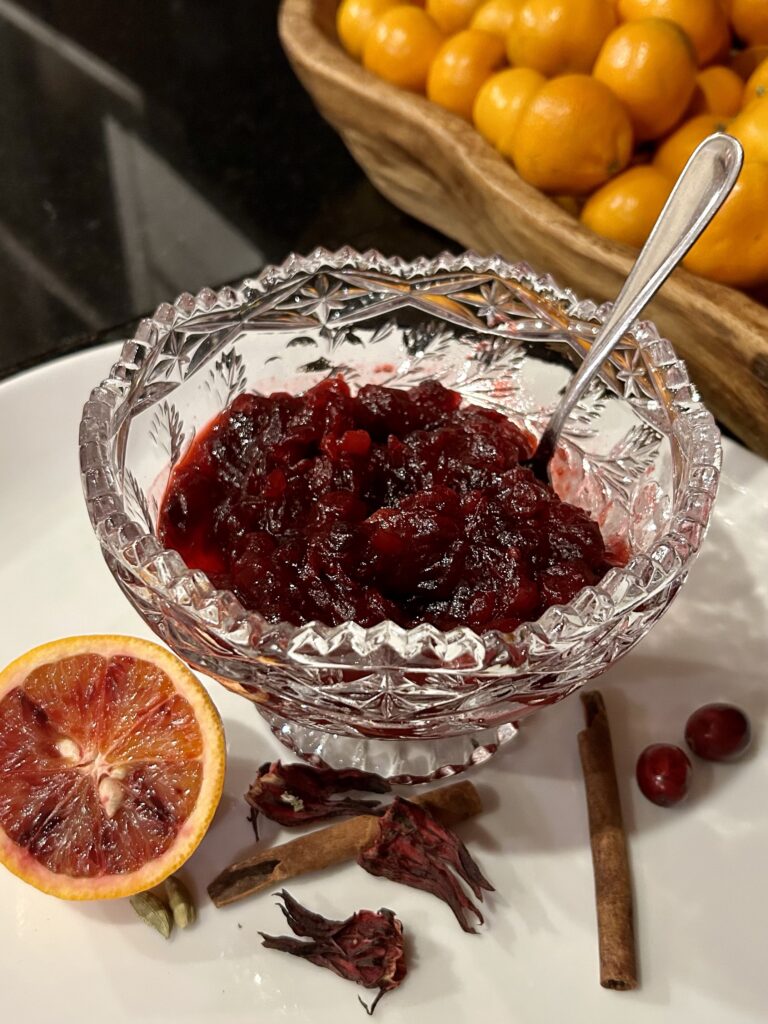 jar of spiced cranberry hibiscus sauce with spices and sliced oranges