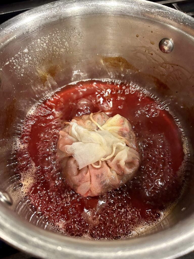 a pan with spiced cranberry hibiscus syrup and a cheesecloth bundle