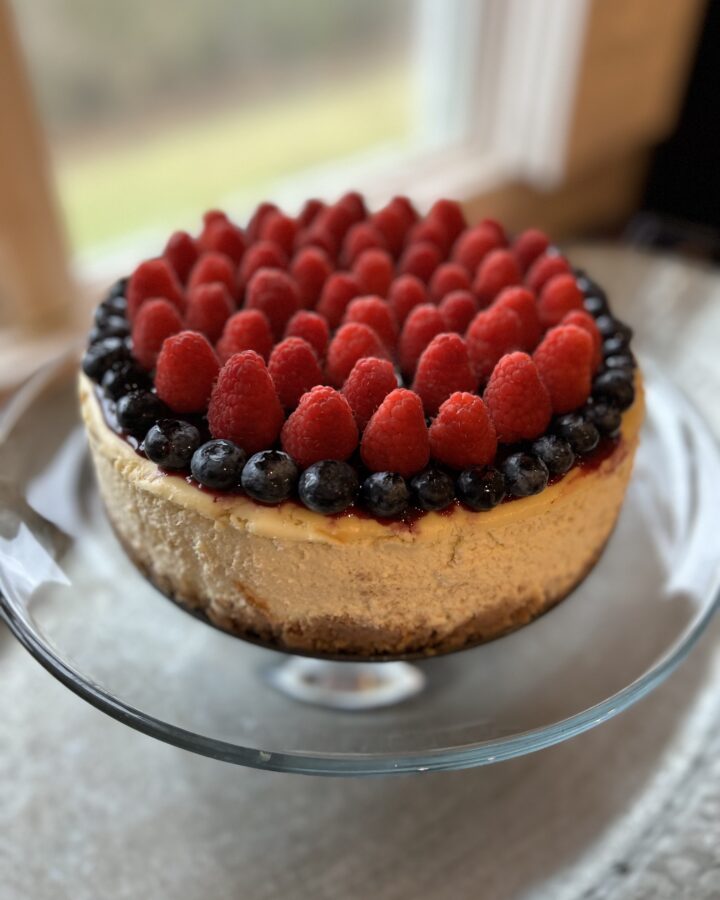 cheesecake on a glass pedestal with fresh berries