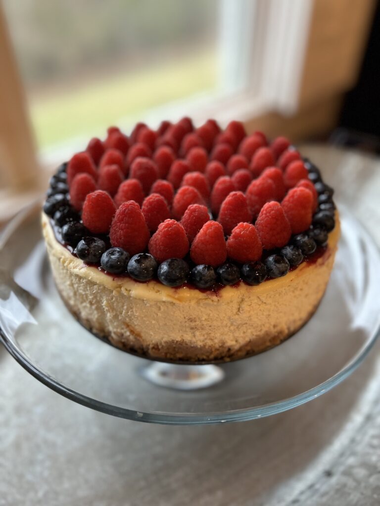 cheesecake on a glass pedestal with fresh berries