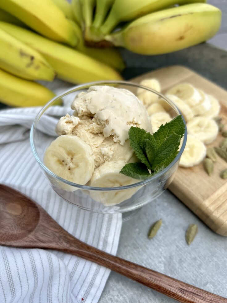 a bowl of banana cardamom ice cream with a wooden spoon, bananas, and a sprig of mint