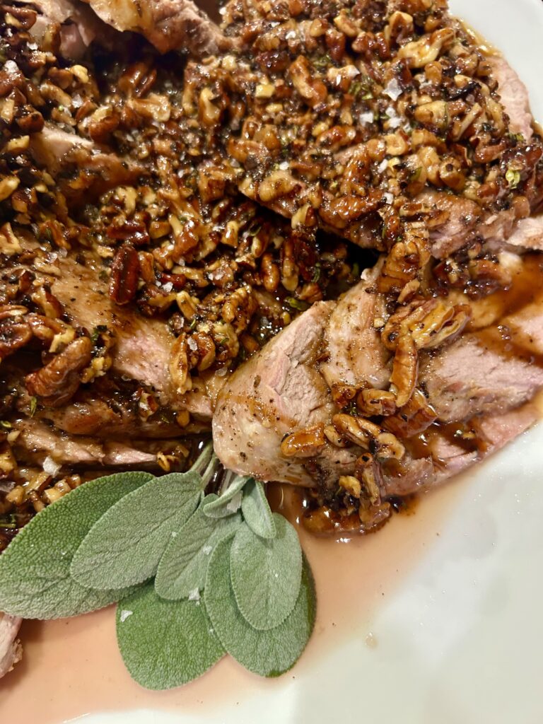 a plate of pork tenderloin sliced with maple pecan sauce poured over garnished in sage leaves