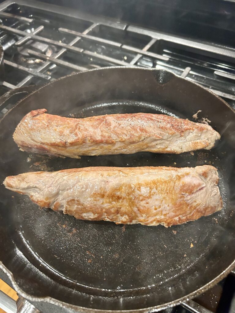 2 pork loins searing in a cast iron pan