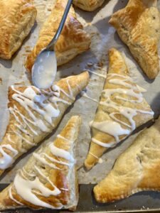glazing a tray of apple turnovers with a spoon and powdered sugar and cream glaze