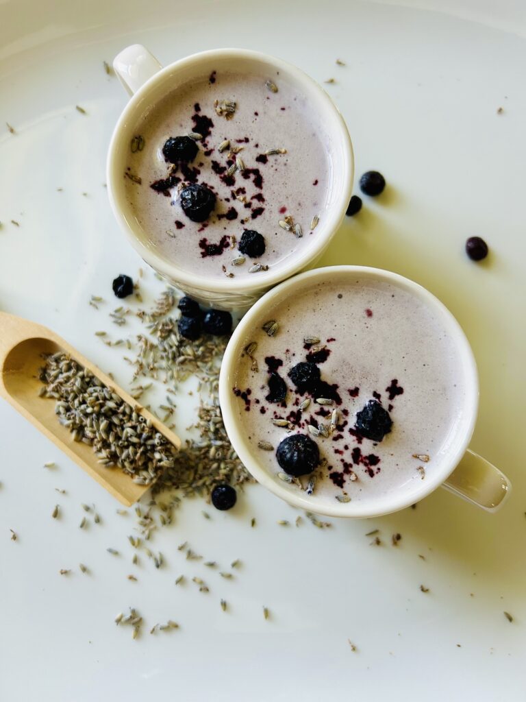 2 mugs of lavender blueberry moon milk on a white platter with lavender scoop